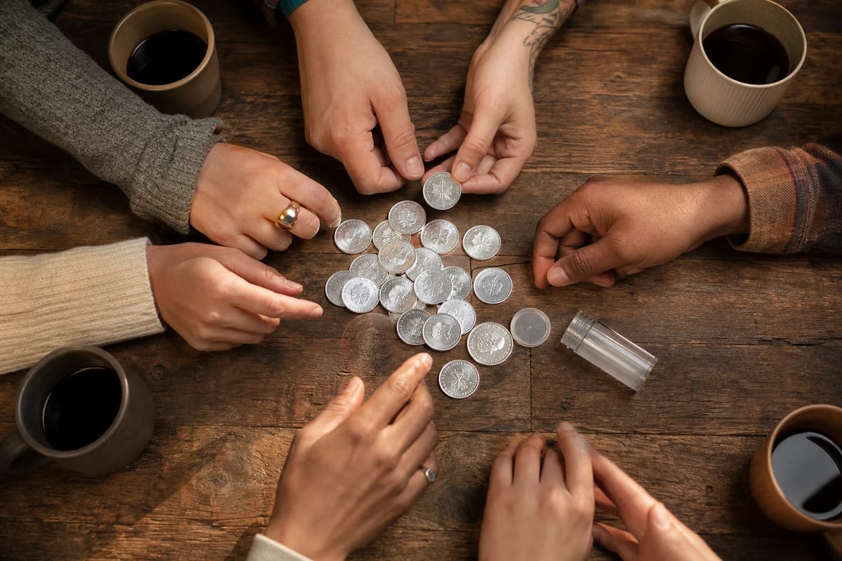Different hands around a table sharing a spread of silver coins